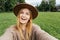 Beautiful young hipster woman taking selfie on green grass at the park. Looking at camera and smile. Travel and active