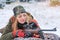 A beautiful young hunter woman in camouflage lies on the ground and looks into the rifle. Winter season and snowy landscape