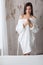 Beautiful young lady in bath robe going to take a bath in white bathroom