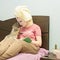 Beautiful young lady sitting on the bed, enjoying beauty procedures at home.  Woman applying a face sheet mask, and reading a book