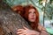 Beautiful young lovely, sexy, red-haired girl. Redhead, smiling, thoughtfully, hugs thoughtfully on a gray tree trunk