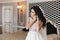 Beautiful young model woman with wedding hairstyle and with trendy makeup puts on her earring in classic luxury interior