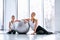 Beautiful young mother sits together with her daughter on the floor near fitball and they keep dumbbells in their hands, at the