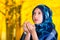 Beautiful young muslim woman wearing blue colored hijab, facing camera folding hands performing muslim prayer, autumn