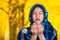 Beautiful young muslim woman wearing blue colored hijab, facing camera folding hands performing muslim prayer, autumn