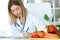 Beautiful young nutritionist working at desk and writing medical records over fresh fruit in the consultation.