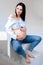 Beautiful young pregnant woman brunette in blue jeans hugs belly on white background