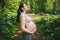 Beautiful young pregnant woman doing yoga exercising in park outdoor. Sitting and relaxing on pink yoga mat. Active future mother