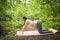 Beautiful young pregnant woman doing yoga exercising in park outdoor. Sitting and relaxing on pink yoga mat. Active future mother