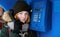 Beautiful young redhead girl in cold season outfit using street blue payphone.