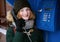 Beautiful young redhead girl in cold season outfit using street blue payphone.