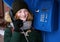 Beautiful young redhead girl in cold season outfit using street blue payphone.