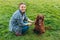 Beautiful young redhead woman playing with happy irish Setter dog in a park outdoors. Girl sitting on a green grass with