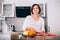 Beautiful young sincerely smiling female chopping grapefruit using a knife and cutting board in modern kitchen. Plenty of apples,