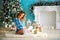 Beautiful young slim smiling pregnant woman in a plaid shirt open unpacking gifts near the Christmas tree and fireplace