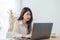 Beautiful young smiling Asian woman working on laptop while at home in office work space.