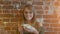 Beautiful young smiling woman with cup of hot coffee standing near brick wall