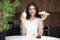 Beautiful young smiling woman feeling hungry holding croissant and glass of yogurt for breakfast in the kitchen looking