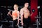 Beautiful young sporty couple showing muscle and posing with dumbbells in gym during photoshooting