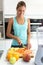 Beautiful young sporty woman cutting some vegetables and fruits while listening to music in the kitchen.