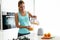 Beautiful young sporty woman serving detox orange juice into glass while listening to music in the kitchen.