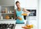 Beautiful young sporty woman serving detox orange juice into glass while listening to music in the kitchen.