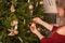 A beautiful young woman adorns a Christmas tree at home.