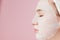 Beautiful young woman is applying a cosmetic tissue mask on a face on a pink background. Healthcare and beauty treatment and