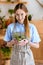 beautiful young woman in apron holding succulents in pots and smiling at camera