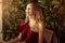 A beautiful young woman in an asymmetrical red-burgundy cocktail dress on one shoulder sits in a restaurant and happily