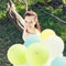 Beautiful young woman with balloons sitting on tree