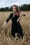 A beautiful young woman in a black dress enthusiastically plays the violin in a wheat field while the wind blows her gorgeous hair