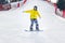 Beautiful young woman in a black helmet and yellow jacket practices snowboarding