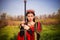 A beautiful, young woman in a black and red medieval dress with a crown on her head stands in a field with a sword in her hands. C