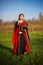 A beautiful, young woman in a black and red medieval dress with a crown on her head stands in a field with a sword in her hands. C