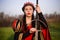 A beautiful, young woman in a black and red medieval dress with a crown on her head stands in a field with a sword in her hands. C