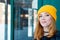 Beautiful young woman with blonde hair and blue eyes in a yellow knitting hat on a background of green wall.