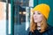 Beautiful young woman with blonde hair and blue eyes in a yellow knitting hat on a background of green wall.