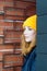 Beautiful young woman with blonde hair and blue eyes in a yellow knitting hat is looking from the corner.