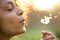 Beautiful young woman blowing dandelion flower