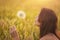 Beautiful young woman blows dandelion in a wheat field in the summer sunset. Beauty and summer concept