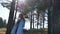 Beautiful young woman in blue coat standing in forest in windy weather autumn sunny day