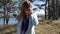 Beautiful young woman in blue coat walking down path in autumn forest in windy weather