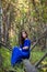 Beautiful, young woman in a blue dress is sitting on a fallen tree in the background of a forest and dry twigs.