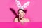 Beautiful young woman with bunny ears and pink blank poster. Funny emotions, excited expressing.