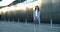 A beautiful young woman in business clothes is standing on a modern street with glass houses. The woman is waiting for