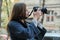 Beautiful young woman with camera in city. Tourist girl traveling and photographing, spring city street background