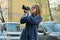 Beautiful young woman with camera in city. Tourist girl traveling and photographing, spring city street background