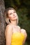 Beautiful young woman with clean perfect skin wearing a classy yellow evening dress against a tree in a natural