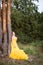 Beautiful young woman with clean perfect skin wearing a classy yellow evening dress, leaning against a tree in the